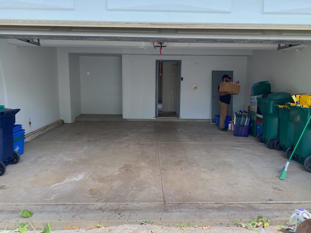 Man Carrying a Box Out of a Cluttered Garage with Trash Bins