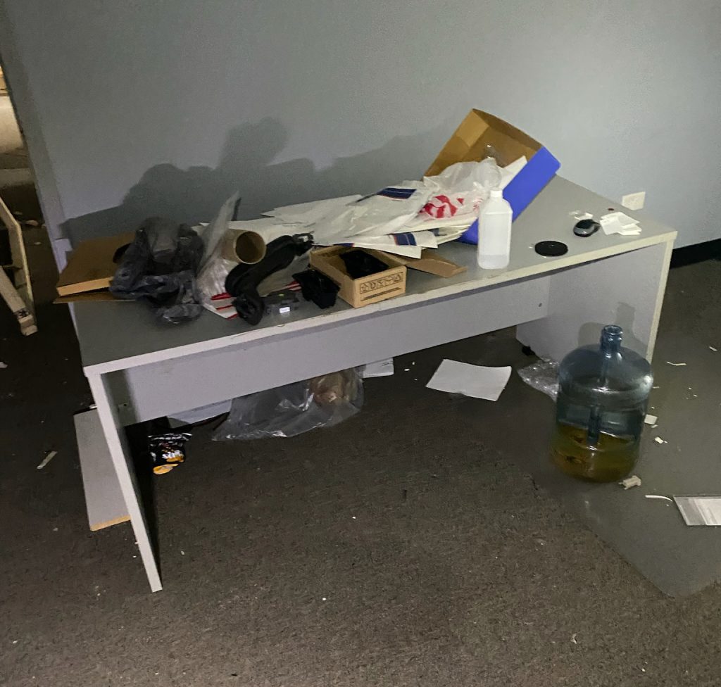 Messy Office Desk Cluttered with Trash, Papers, and a Large Water Jug